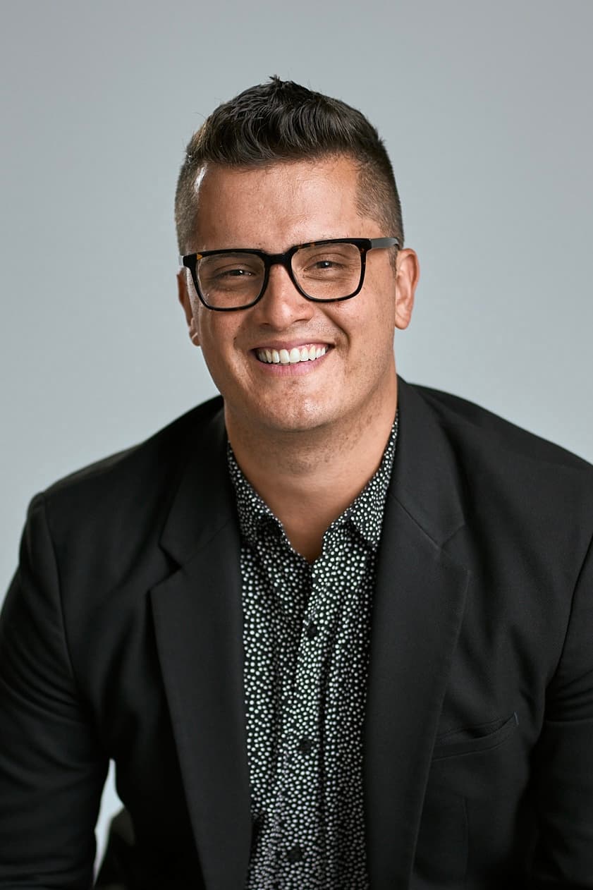 Nik Vassev, chest-up studio portrait in a black blazer and glasses.